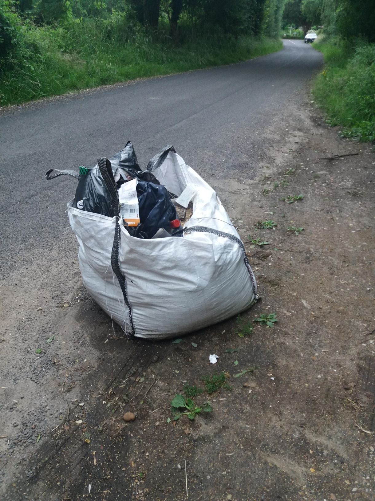 Large builders’-type bag containing household waste and wood shavings fly-tipped into the layby